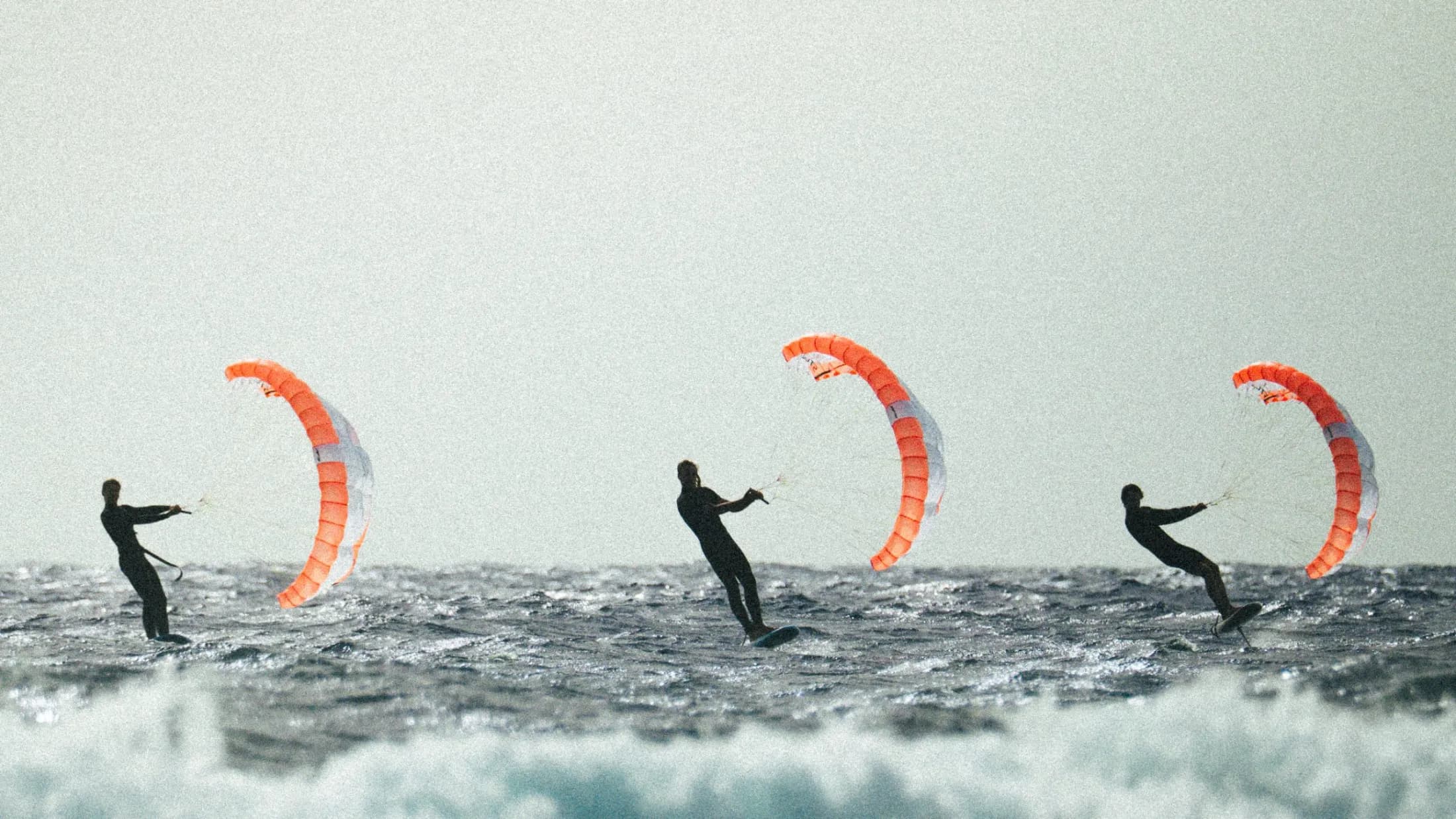 Tres riders practicando parawing foil mar adentro